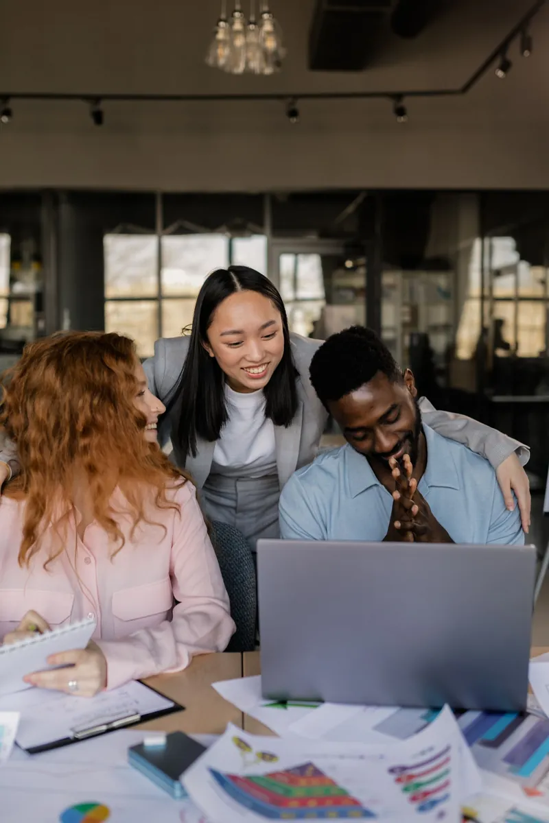 Trois collègues de différentes origines souriant devant un ordinateur